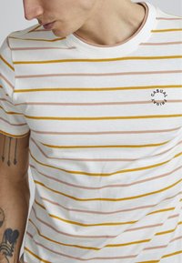 Striped T-shirt in white, featuring horizontal stripes in yellow and light pink. Round neckline, short sleeves, with "CASUAL" logo detail.