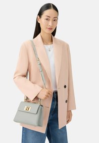 Grijze leren handtas met gouden details, gestructureerde vorm en verstelbare riem. Draagt een lichtroze blazer en blauwe spijkerbroek.