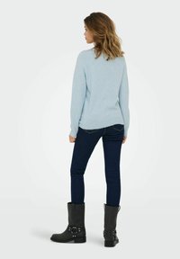 Light blue sweater with a relaxed fit, paired with dark denim jeans and black ankle boots featuring buckle accents.