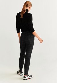 Pull noir côtelé à col roulé associé à un pantalon noir ajusté à carreaux et des baskets noires avec des accents blancs et rouges.