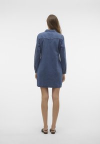 Jeansklänning, långa ärmar, krage, mörkblå, rak skärning, midjehöjd, bakre yoke-detalj, minimal sömnad, bärs med svarta sandaler.