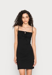 Vestido preto justo com alças finas, corpete franzido e detalhe de laço na parte da frente. Tecido liso e elástico com um design simples e elegante.