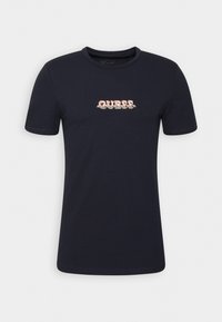 Marineblaue Baumwoll-T-Shirt mit kurzen Ärmeln. Mit dem "GUESS" Logo in Rot und Weiß in der Mitte. Rundhalsausschnitt-Design, glatte Textur.