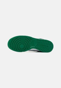 Nike sneakersål med en grøn gummiydersål, der har et cirkulært mønster, tekstureret greb og en kontrasterende hvid mellemsål.
