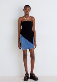 Svart strapless topp kombinert med et denimskjørt med skråsnitt, med en blå og lyseblå gradient, komplementert av kraftige svarte sandaler.