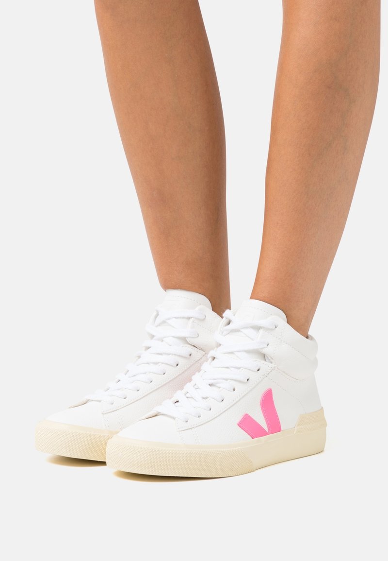 Hvide høje sneakers med pink "V"-logo, båret på fødder, med hvide snørebånd og off-white gummisåler.