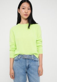 Neon zielony sweter z prążkowanymi mankietami i okrągłym dekoltem, zestawiony z jasnoniebieskimi, wysokim stanem dżinsami z paskiem.