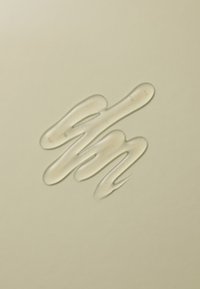 En klar geléaktig substans sprer seg i et abstrakt, bølgete mønster på en lys beige bakgrunn, og viser en glatt, blank tekstur.