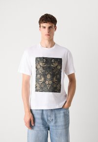Weißes Baumwoll-T-Shirt mit einem dunkel gemusterten rechteckigen Grafikdesign mit goldenen Akzenten, das Vögel und florale Motive darstellt.