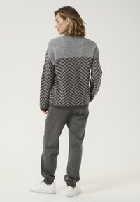 Grau gemusterter Pullover mit Fischgrätmuster auf dem Rücken, kombiniert mit grauen Hosen und weißen Sneakers. Weicher Stoff, lockere Passform.