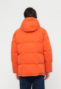 Orange puffer jacket with a hood, featuring horizontal quilted design and a loose fit. Plain texture, no visible hardware or accents.