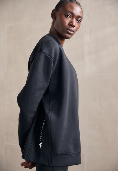 Sweatshirt noir en tissu doux, présentant un design décontracté, des manches longues et un accent logo sur le côté. Texture lisse avec une coupe décontractée.