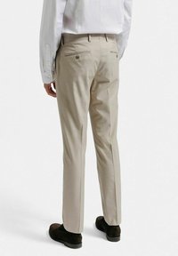 Beige skräddarsydda byxor med en slät textur, med två bakfickor och subtila knappdetaljer. Bärs med en vit skjorta och mörka skor.