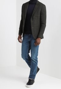 Šedý vlněný blazer s klopami, nošený přes námořnický rolák, spárovaný s modrými džíny a černými teniskami. Viditelná horní část těla a nohy.