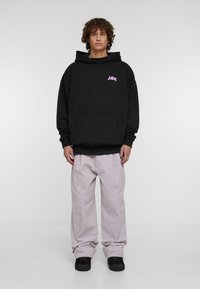 Melnā kokvilnas kapuci ar garām piedurknēm, kangaro somu un rozā logotipu uz krūtīm. Saskaņots ar gaiši violetiem brīviem biksēm.