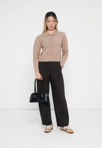 Beige strikket genser med krage, brune vide bukser, svart veske og mønstrede joggesko med lys såle.