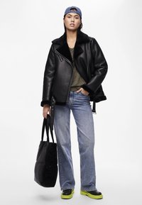 Svart lærjakke med pelskrage, grønn skjorte, lyseblå jeans, svart puffet totebag og svarte og grønne klumpete støvler.