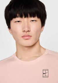 Camiseta deportiva de color rosa claro, fabricada en tejido transpirable, con mangas cortas y un logo negro de Nike en la parte superior izquierda.