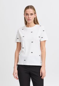 White cotton t-shirt featuring scattered black bow embroidery. Crew neck, short sleeves, relaxed fit, smooth texture, no visible hardware.