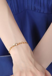 Gold bracelet featuring butterfly motifs and small clear stones, intricately linked, on a slender chain. Worn on a wrist with light skin tone.