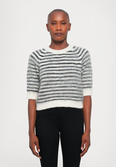 Maglione a righe in morbido e peloso materiale, con righe orizzontali bianche e nere, collo a giro e maniche corte. Abbinato a pantaloni neri.