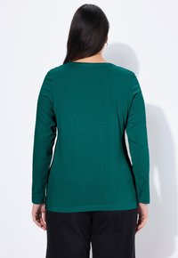 Długi rękaw w kolorze morskim, wykonany z miękkiej, elastycznej tkaniny, z okrągłym dekoltem i standardowym wykończeniem, widoczny z tyłu z gładkimi konturami.