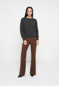 Γκρι υπερμεγέθης πουλόβερ με ριμπ μανσέτες, συνδυασμένο με καφέ παντελόνι με καμπάνα. Το μοντέλο φοράει μαύρες γόβες με μυτερή μύτη. Ουδέτερο φόντο.