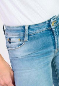 Jean en denim bleu clair à coupe slim, taille mi-haute, fermeture à bouton et décoloration subtile avec poches avant.