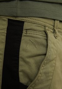 Olivgrön cargobyxor med en svart sidostripe, framfickor och synliga sömmar. Tyget är mjukt med en lätt struktur.