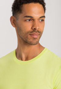 Lys gul bomulds t-shirt med rund hals, tæt siddende, der viser en glat tekstur og simpelt design, båret af en person med kort, krøllet hår.