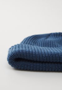 Beanie tricotat albastru, cu textură ribbed, margine răsucită și un material moale, flexibil. Designul include linii orizontale pronunțate.