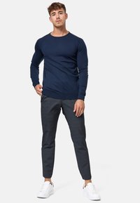 Chemise à manches longues navy avec col rond, associée à un pantalon texturé gris foncé et des baskets blanches. Coupe décontractée avec des poignets côtelés.