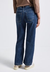 Jean en denim bleu foncé avec une coupe décontractée, dotés de poches arrière, d'une taille mi-haute et d'une jambe droite. Le tissu a une texture lisse.