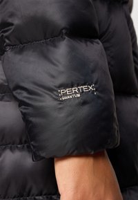 Kadar crne jakne s punjenjem koja prikazuje rukav s logom "Pertex Quantum", naglašavajući njegovu teksturiranu tkaninu i usko pristajanje.