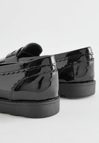 Svarta lackläderloafers med platt sula, som har skulpterade detaljer längs kanterna och en slät, glänsande finish.