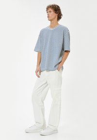 Stribet blå og hvid T-shirt med korte ærmer og rund halsudskæring, parret med løstsiddende hvide cargo-bukser og hvide sneakers.