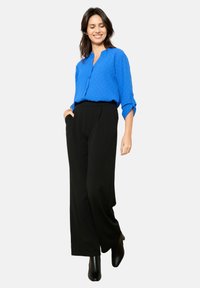 Blusa blu con bottoni e piccoli pois, abbinata a pantaloni neri palazzo a vita alta e stivaletti neri. Texture lisce in tutto il look.