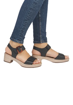 Schwarze Ledersandalen mit einem breiten Riemen, verstellbarem Schnallenverschluss und einem klobigen, strukturierten, beigen Absatz. Offene Zehen.