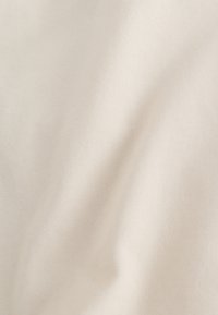 Close-up of soft, light beige fabric with a subtle diagonal weave pattern and slight folds creating gentle shadows.