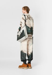 Conjunto de ropa multicolor con estampado de paisaje; incluye una camiseta de manga larga y pantalones a juego con puños elásticos. Botas marrones y un bolso tote.