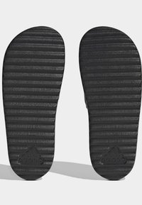 Sorte gummisål til sandaler med vandrette riller, der har et præget logo. Tekstureret overflade for greb og stabilitet.