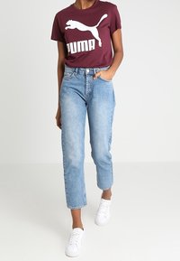Maroon cotton t-shirt with white 'PUMA' logo, paired with light blue straight-leg jeans and white sneakers. Casual fit, short sleeves.
