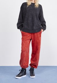 Sweatshirt in verblasstem Schwarz, mit Rundhalsausschnitt und lockerer Passform. Kombiniert mit lockeren roten Sweatpants und hohen schwarzen Sneakers.