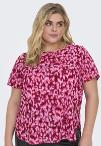 Blusa rosa a maniche corte con stampa leopardata astratta in diverse sfumature di rosso e rosa. Tessuto morbido, vestibilità rilassata e spacchi laterali.
