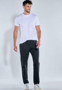 Weißes T-Shirt mit kurzen Ärmeln aus Baumwolle, kombiniert mit dunkelgrauen Jogginghosen mit Kordelzug, präsentiert mit weißen Sneakern. Einfacher und entspannter Schnitt.