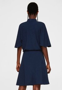 Robe bleu marine à manches courtes, coupe trapèze, texture lisse et design minimaliste. Elle présente une fermeture au dos et une silhouette fluide.