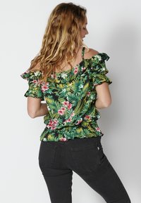 Top floreale off-the-shoulder con foglie verdi e fiori rosa su uno sfondo nero. Maniche arricciate e vita aderente.