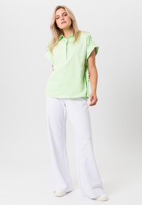 Lichtgroen polo-shirt met korte mouwen en kraag, gecombineerd met witte wijde broek, tegen een neutrale achtergrond.