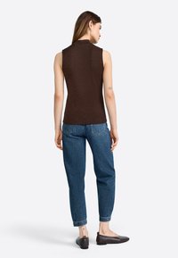 Brown sleeveless top with a ribbed texture, paired with relaxed blue denim jeans, and brown flat shoes. Rear view, simple design.