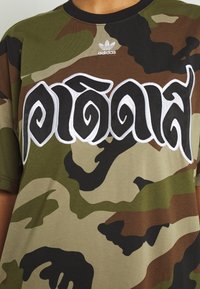 Camo pattern t-shirt in shades of green, brown, and black. Features a white embroidered text design and a black crew neck.